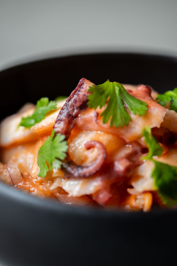 Close-up of a vibrant seafood dish featuring tender octopus slices, garnished with fresh cilantro leaves, served in a black bowl.